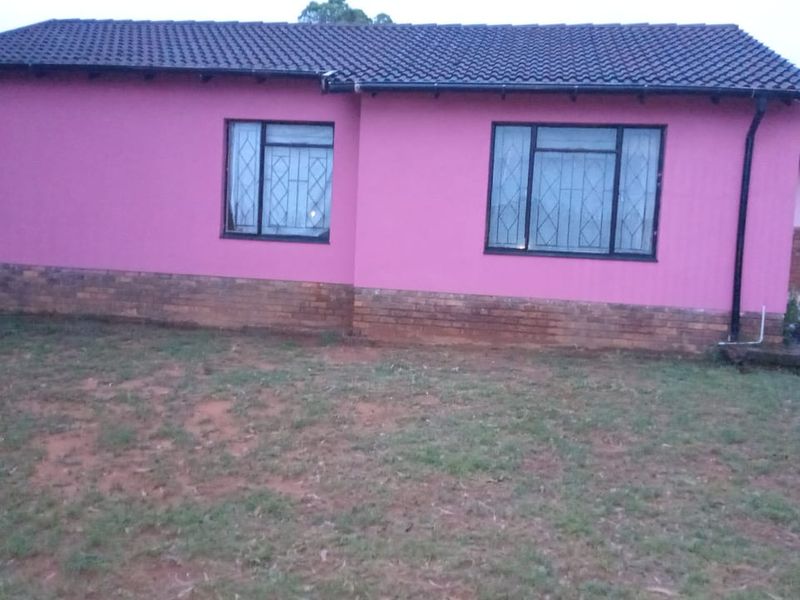 Rear view of a single-story house featuring a tiled roof, brick plinth base, and security bars on the windows.