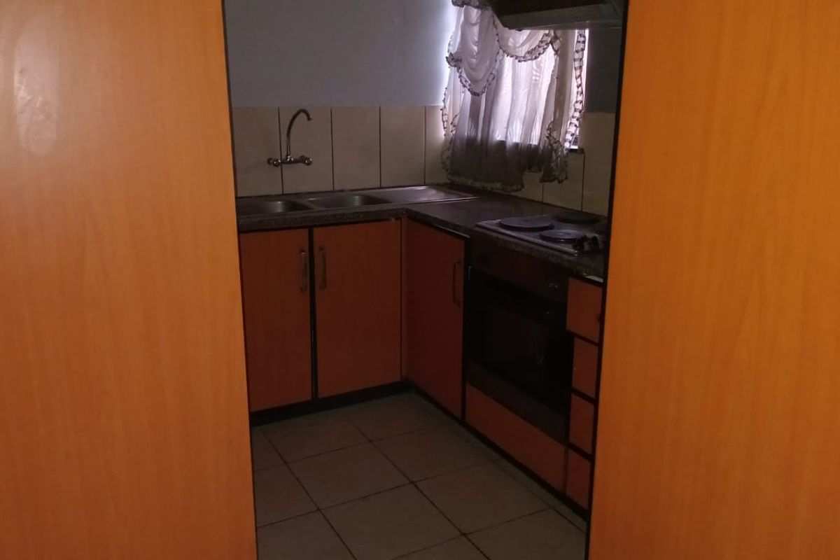 A compact kitchen featuring built-in wooden cabinetry, a double sink, an electric hob, and an integrated oven with tiled flooring and backsplash.