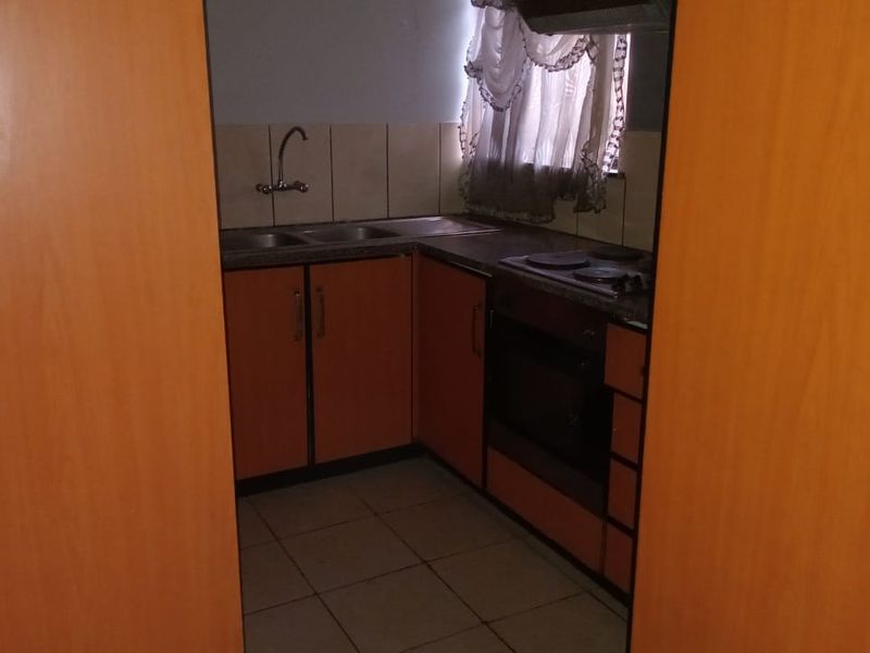 A compact kitchen featuring built-in wooden cabinetry, a double sink, an electric hob, and an integrated oven with tiled flooring and backsplash.