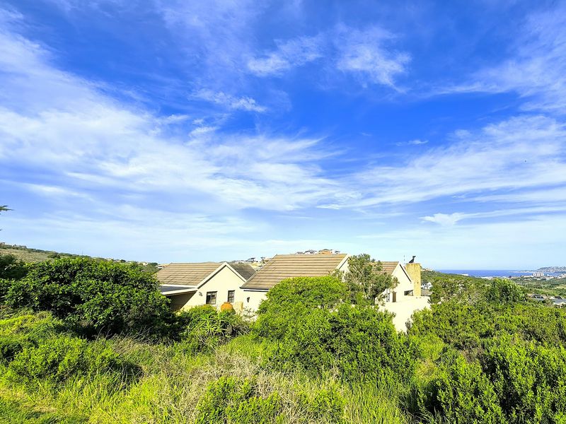 A rear view of the property featuring a tiled roof and chimney, set within a lush, landscaped garden environment with distant coastal views.