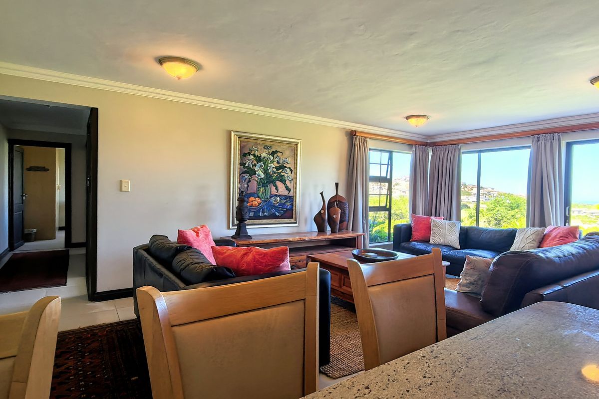 Spacious living room featuring large windows with natural light, tiled flooring, and ceiling cornices, offering a comfortable and bright atmosphere.