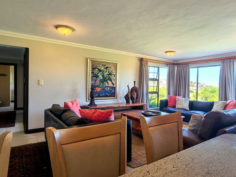 Spacious living room featuring large windows with natural light, tiled flooring, and ceiling cornices, offering a comfortable and bright atmosphere.