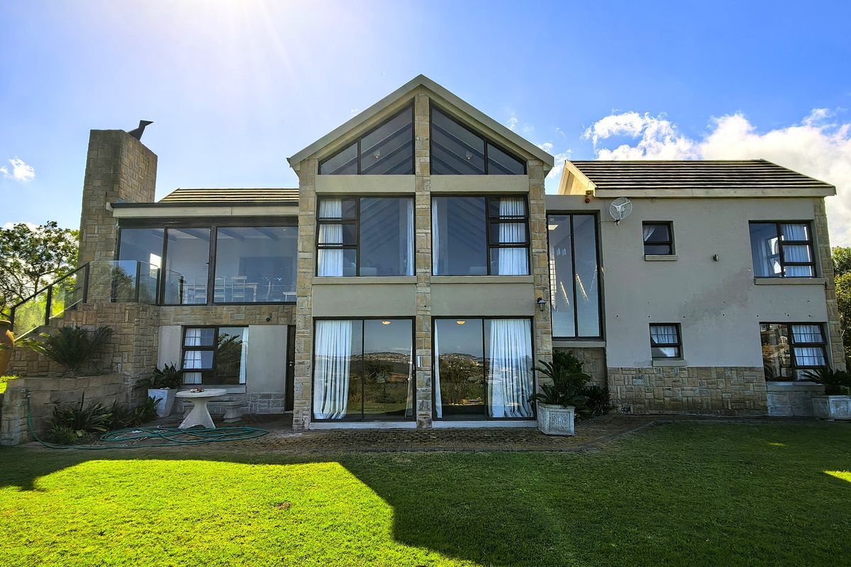 Rear elevation of a multi-story house featuring extensive glass windows, stone cladding, and a paved patio overlooking a landscaped garden.