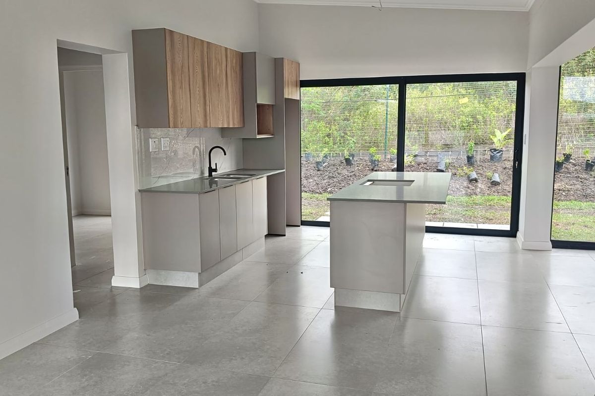 Modern open-plan kitchen featuring sleek cabinetry, a central island with stone countertops, and large sliding doors providing seamless access to the garden.
