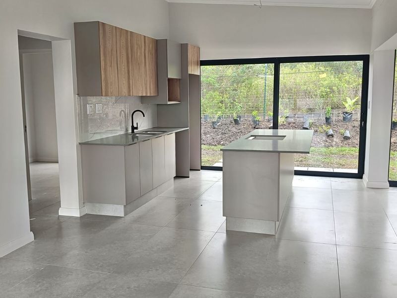 Modern open-plan kitchen featuring sleek cabinetry, a central island with stone countertops, and large sliding doors providing seamless access to the garden.