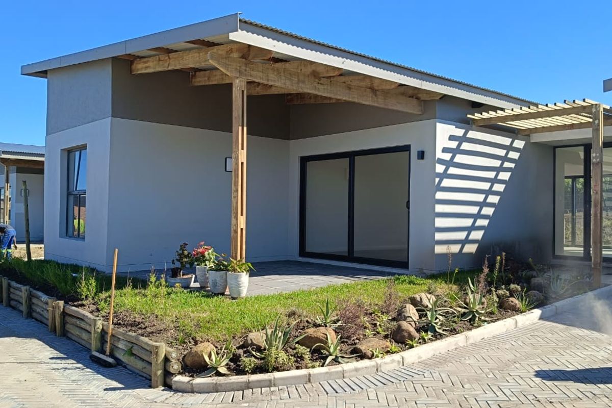 Modern cluster home exterior featuring a covered timber pergola, paved patio area, and landscaped garden beds with sliding door access.