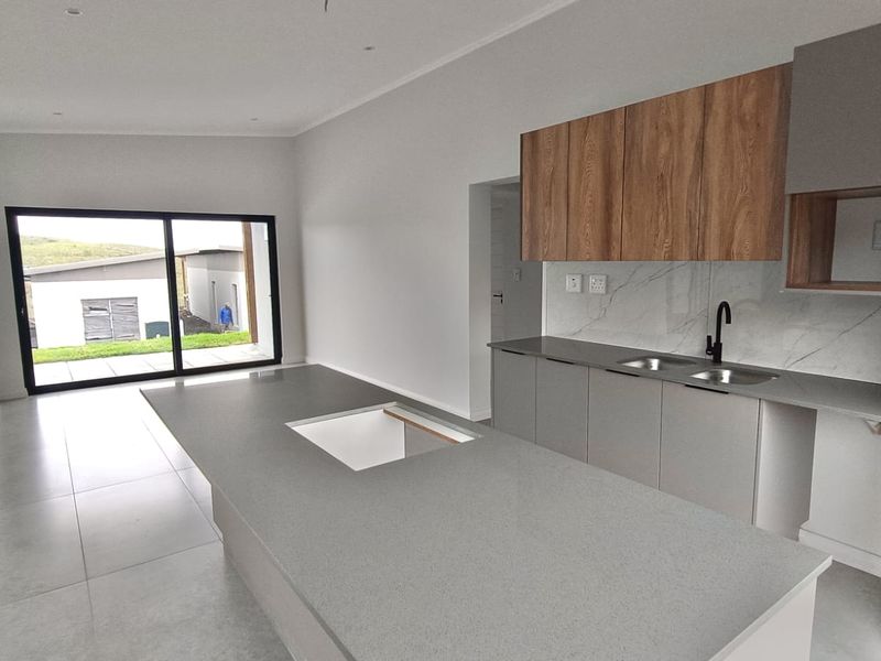 Modern open-plan kitchen featuring a large island, stone countertops, wood-finish cabinetry, and sliding glass doors leading to the exterior.