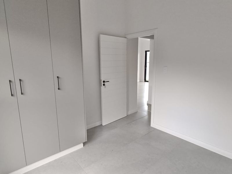 A clean, modern bedroom featuring neutral tiled flooring and ample built-in cupboard storage, presenting a bright and well-maintained living space.