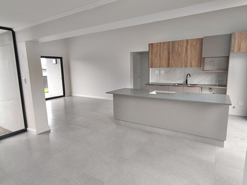 Modern open-plan living area featuring a sleek kitchen with stone countertops, wood-finish cabinetry, and large sliding glass doors leading to the exterior.