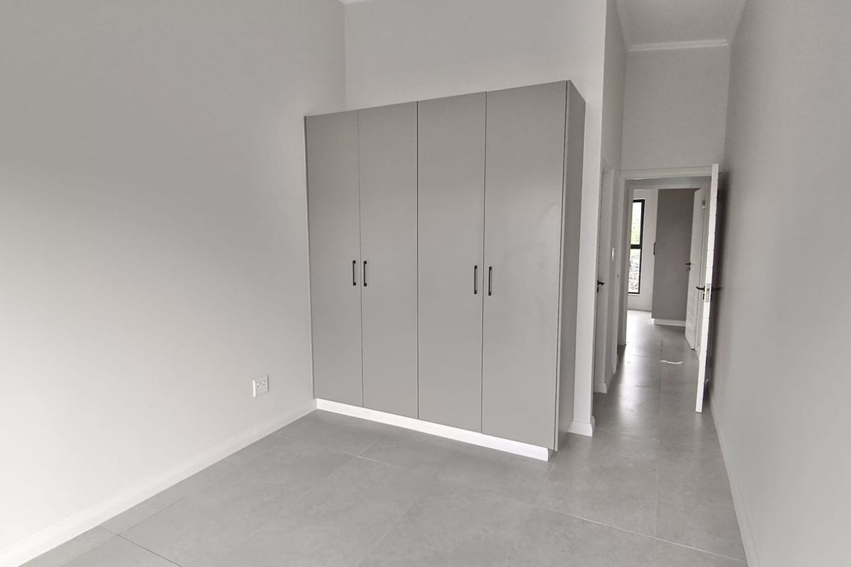 A bright, modern bedroom featuring neutral grey floor tiles and sleek, built-in cupboards, offering a clean and minimalist living space.