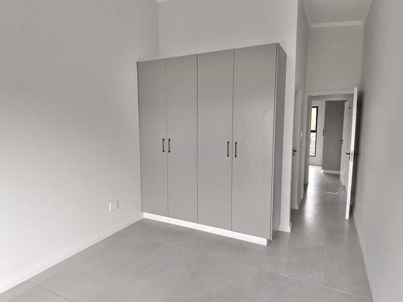 A bright, modern bedroom featuring neutral grey floor tiles and sleek, built-in cupboards, offering a clean and minimalist living space.