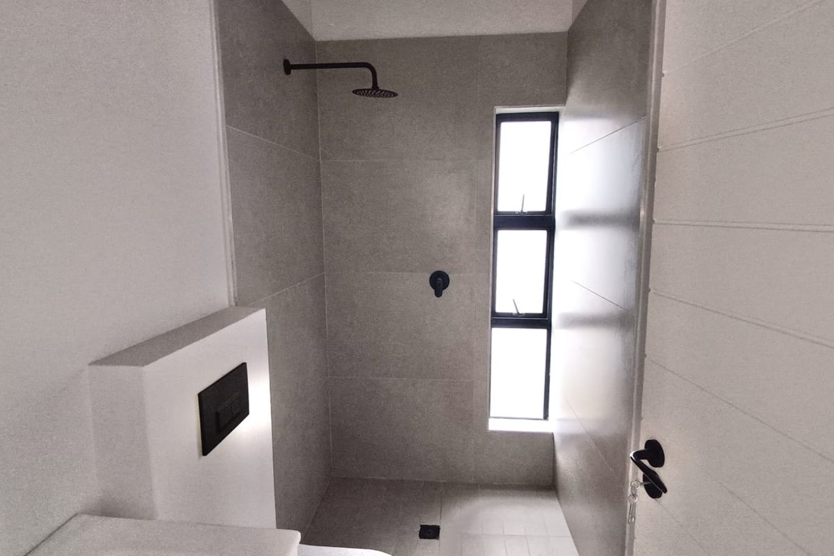 Modern bathroom featuring a walk-in shower with a matte black rain shower head, grey wall tiles, and a concealed cistern toilet.
