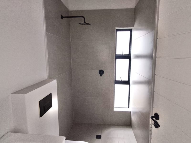 Modern bathroom featuring a walk-in shower with a matte black rain shower head, grey wall tiles, and a concealed cistern toilet.