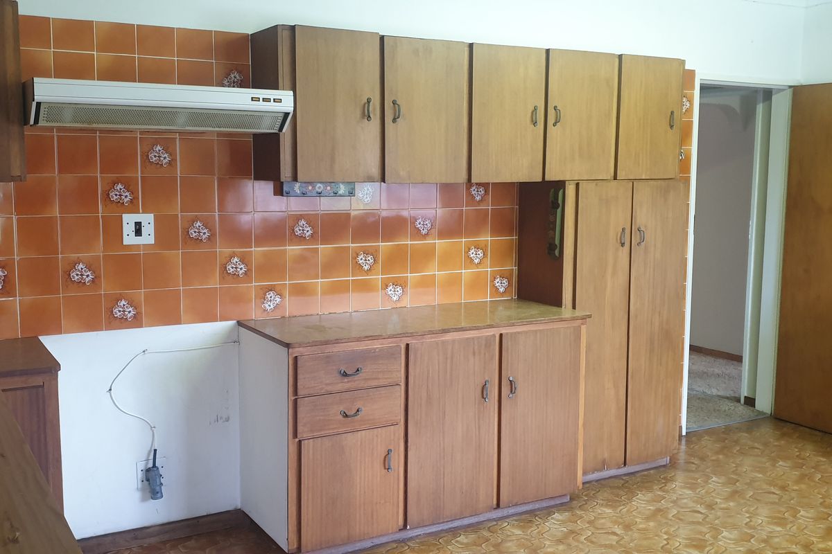A dated kitchen featuring wooden cabinetry, a tiled backsplash, and an extractor fan, currently awaiting a new stove and oven installation.