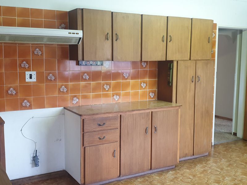A dated kitchen featuring wooden cabinetry, a tiled backsplash, and an extractor fan, currently awaiting a new stove and oven installation.