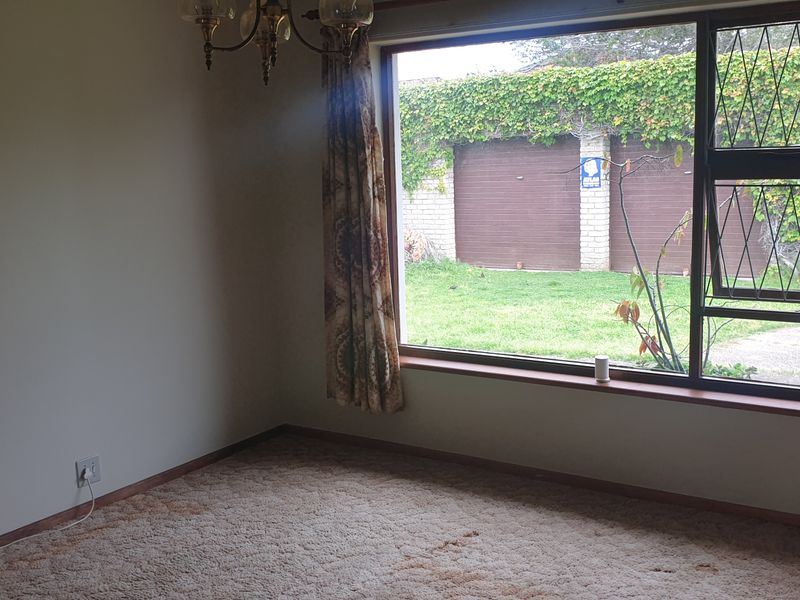An empty living room featuring a large picture window with leaded glass detail, overlooking a rear garden and garage area.