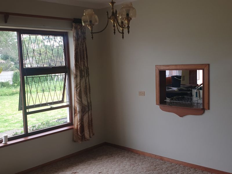 A dining room featuring a large window with garden views and a timber-framed serving hatch connecting to the kitchen area.