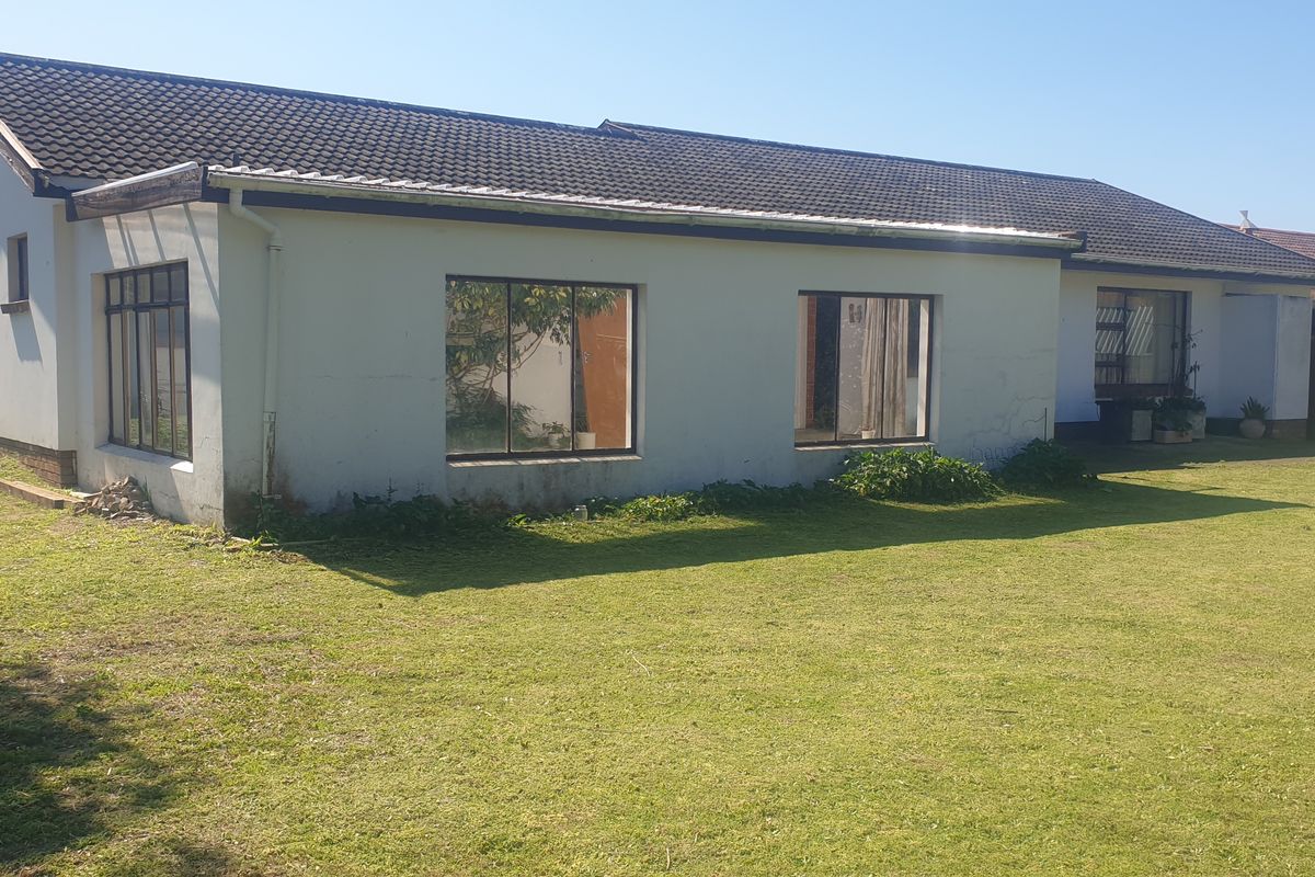Rear view of a single-story residential house featuring a tiled roof, metal window frames, and a large surrounding lawn area.