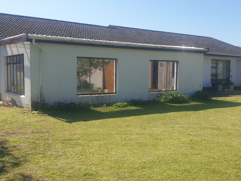 Rear view of a single-story residential house featuring a tiled roof, metal window frames, and a large surrounding lawn area.