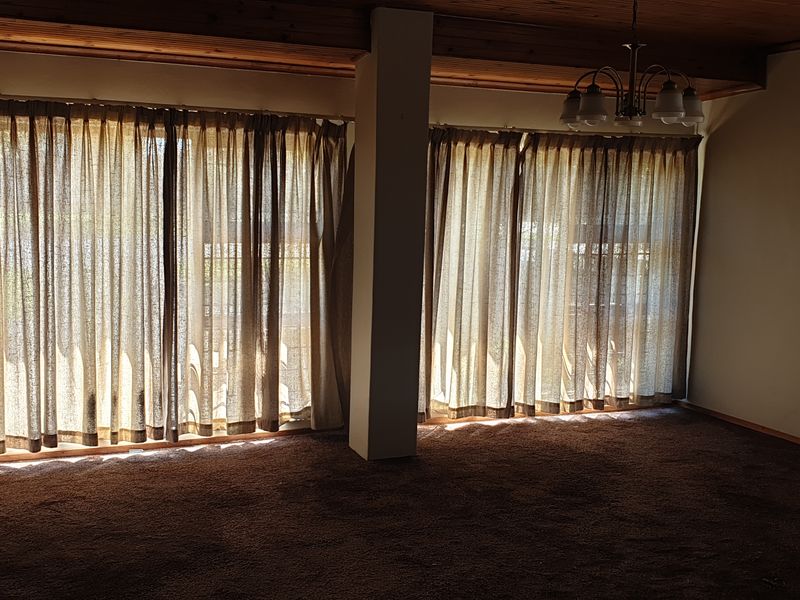 Spacious living area featuring timber ceilings, large sliding glass doors providing natural light, and a central support pillar, ready for modern updates.