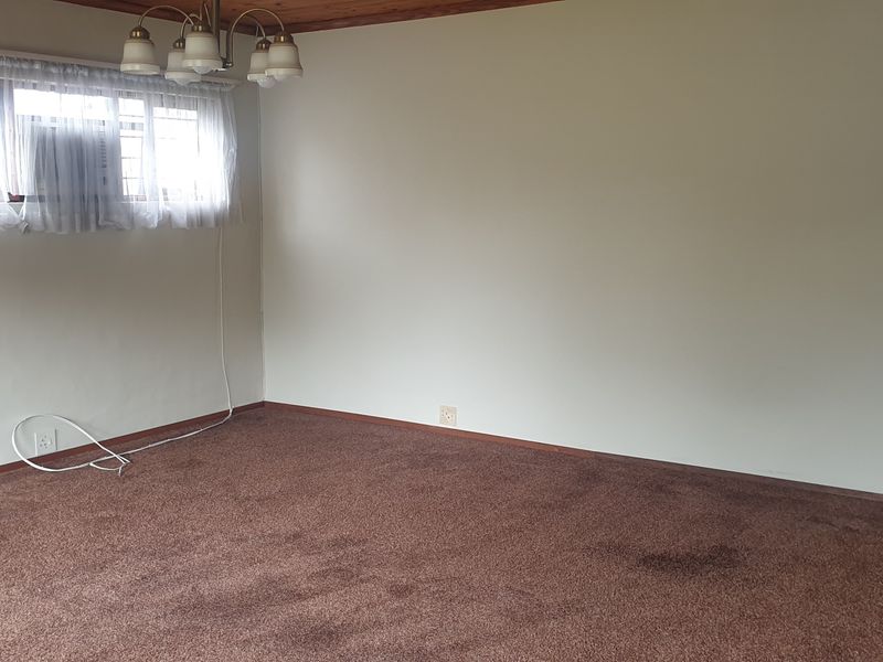 An empty living room featuring brown carpeting, timber ceiling trim, and a window with security bars, offering a blank canvas for renovation.