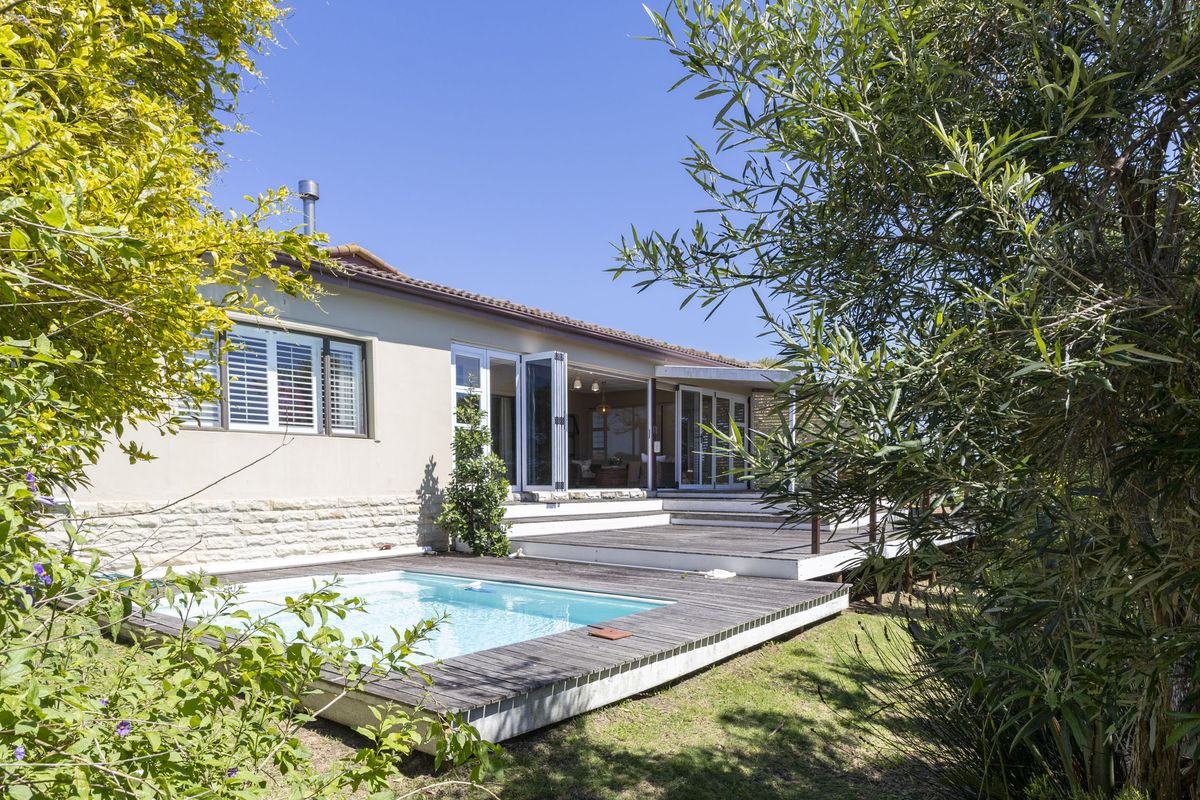 Rear view of the property featuring a swimming pool, expansive timber decking, and large bi-fold doors leading into the living area.
