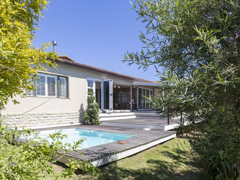 Rear view of the property featuring a swimming pool, expansive timber decking, and large bi-fold doors leading into the living area.
