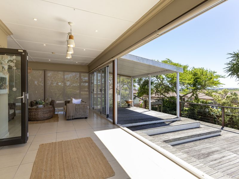 Spacious covered patio featuring tiled flooring and recessed lighting, seamlessly transitioning to an expansive timber deck with cable railings and elevated garden views.