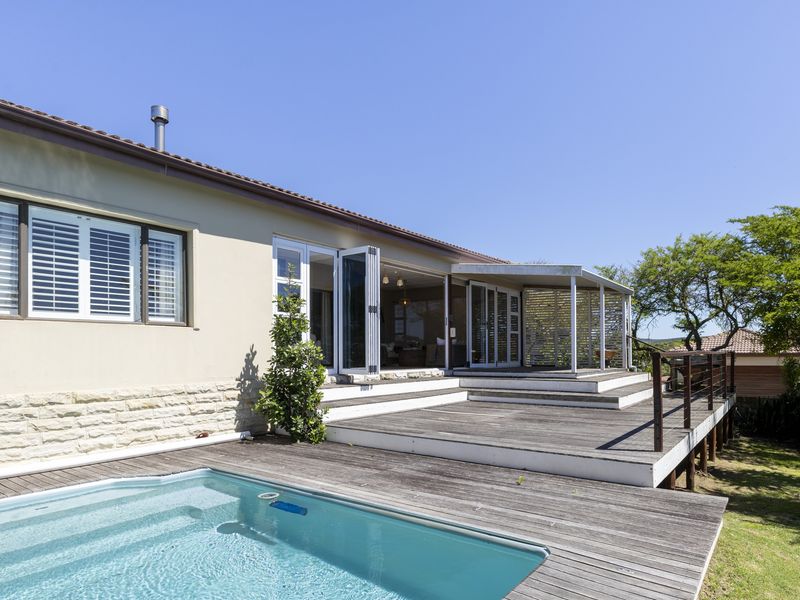 Rear exterior view featuring a swimming pool, multi-level timber decking, and a covered patio area with bi-fold doors leading into the home.