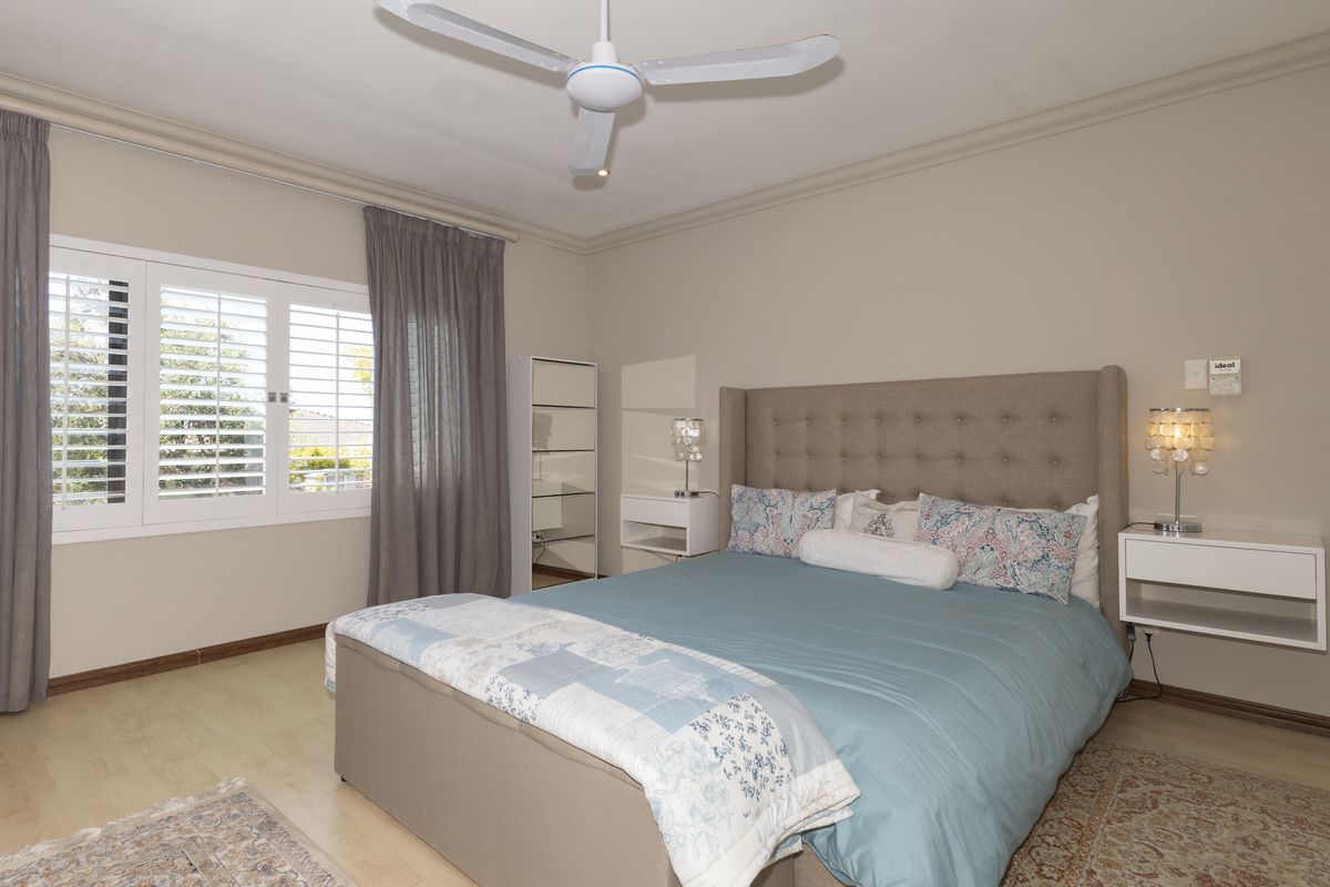 A well-maintained bedroom featuring laminate flooring, plantation shutters, and a ceiling fan, offering a comfortable and functional living space.