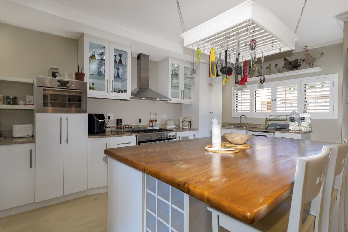 A well-appointed kitchen featuring a large wooden island, stainless steel appliances, glass-fronted cabinetry, and a functional hanging pot rack above the workspace.