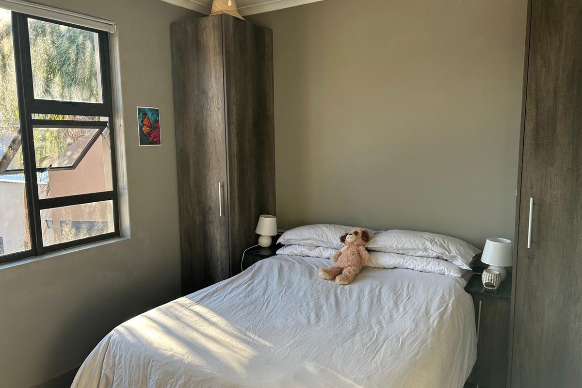 A functional bedroom featuring built-in cupboards and natural light from an aluminium-framed window.