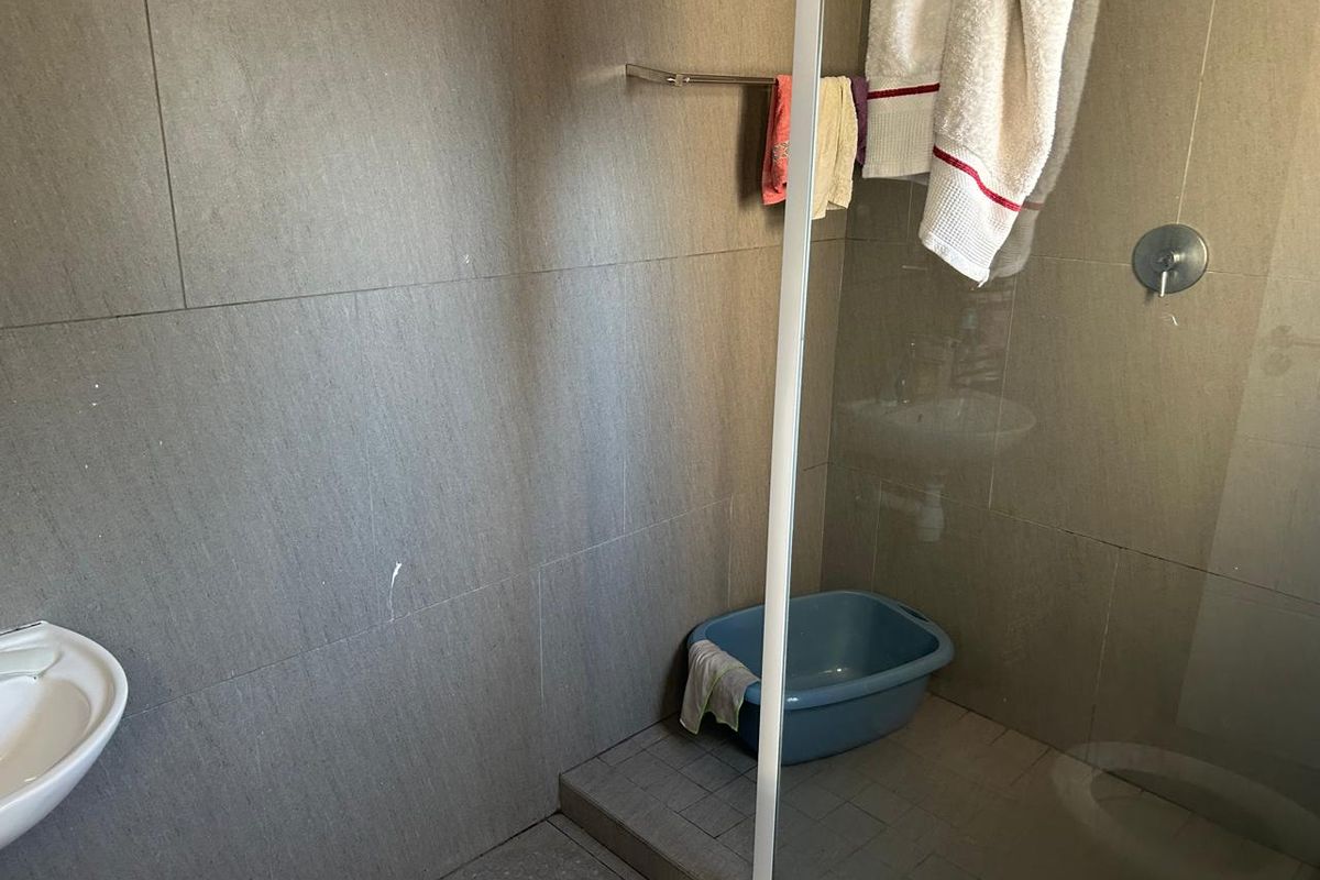 A functional bathroom featuring grey wall and floor tiles, a glass shower enclosure, and a wall-mounted shower mixer.
