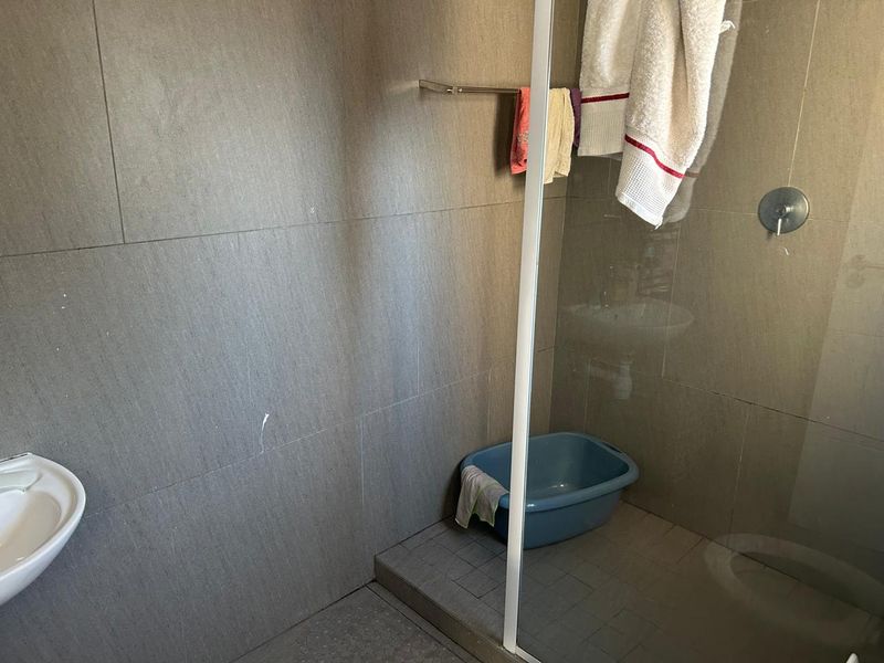 A functional bathroom featuring grey wall and floor tiles, a glass shower enclosure, and a wall-mounted shower mixer.
