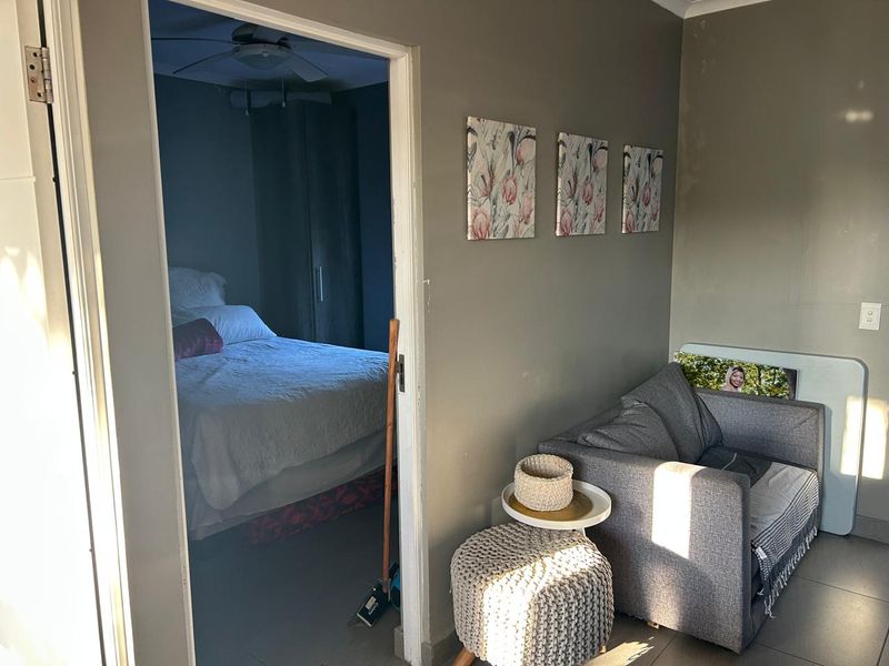 A living area featuring tiled flooring and a ceiling fan, with a view into an adjacent bedroom.
