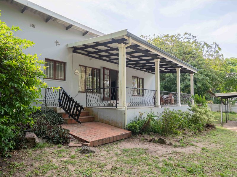 A covered rear patio featuring wrought iron railings, brick steps, and direct access to the garden area.