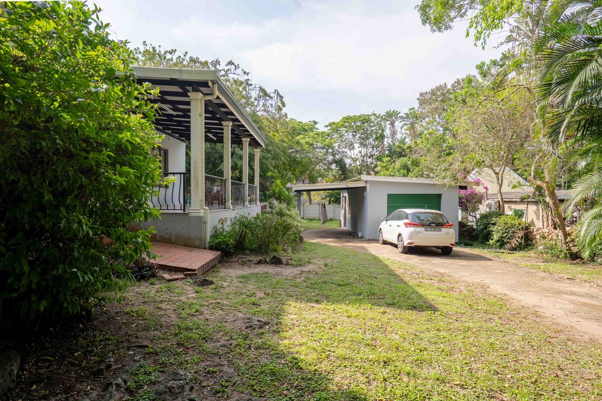 Rear view of the property featuring a covered patio, a detached garage, and a spacious garden area with a driveway.