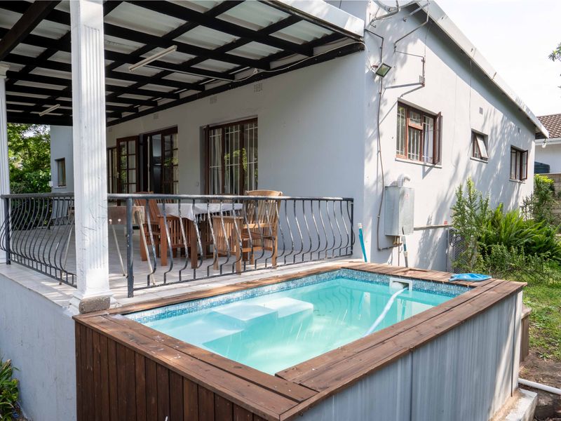 A raised swimming pool with timber decking adjacent to a covered patio area featuring tiled flooring and wrought iron railings.