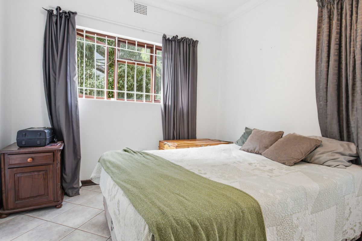 A bedroom featuring tiled flooring, a window with security bars, and ceiling cornicing.