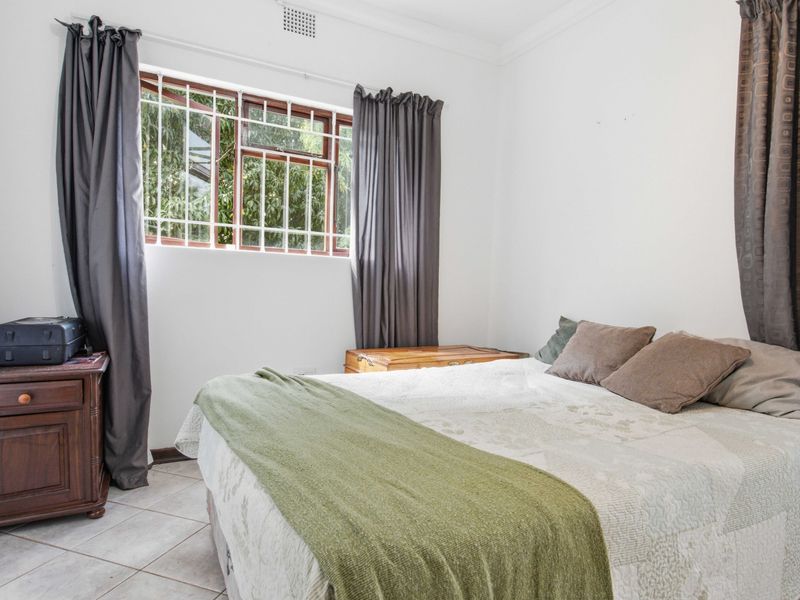 A bedroom featuring tiled flooring, a window with security bars, and ceiling cornicing.