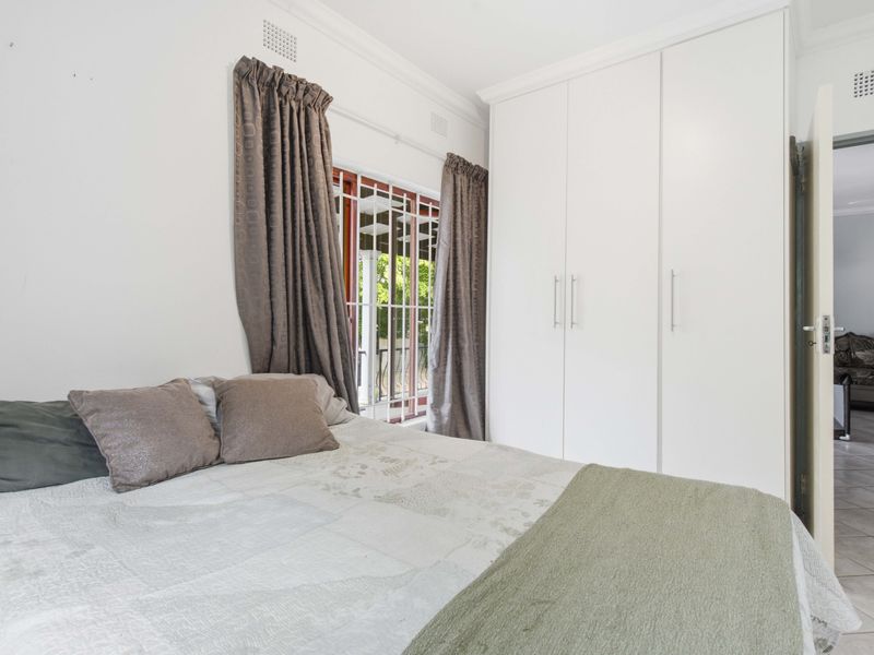 A well-maintained bedroom featuring built-in cupboards, security bars on the window, and neutral finishes, offering a clean and functional living space.