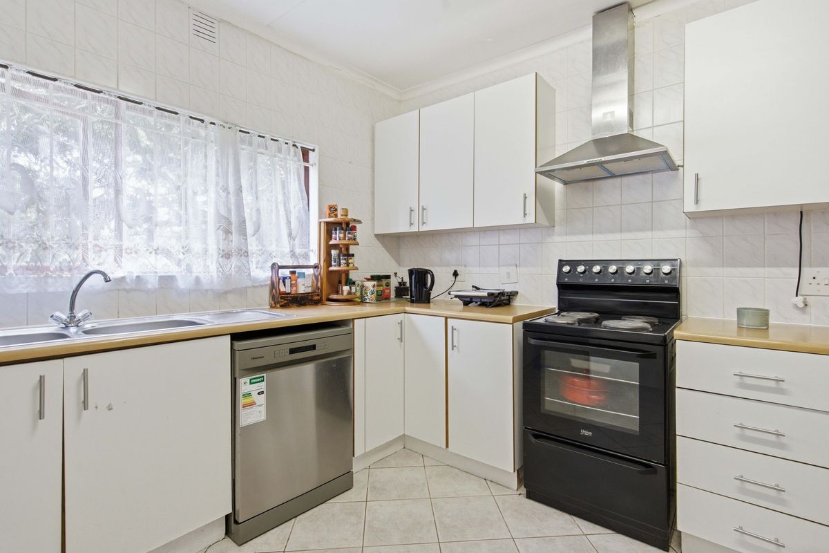 A functional kitchen featuring white cabinetry, tiled splashbacks, a stainless steel sink, and a freestanding oven with an extractor fan.