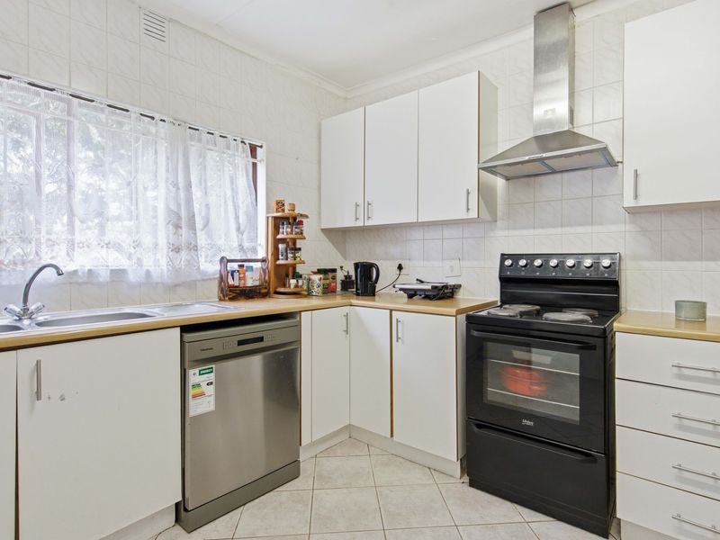 A functional kitchen featuring white cabinetry, tiled splashbacks, a stainless steel sink, and a freestanding oven with an extractor fan.