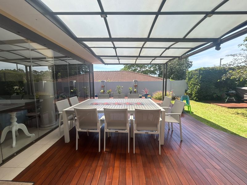 A spacious covered patio featuring timber decking and a modern polycarbonate roof, seamlessly connecting to the interior through large sliding glass doors.