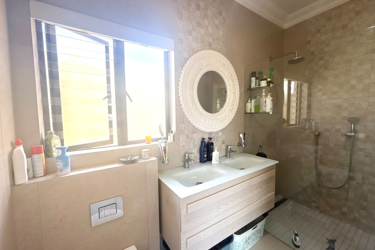 Modern bathroom featuring a double vanity, wall-mounted toilet, and a spacious glass-enclosed shower with mosaic tile accents.