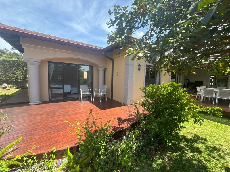 A spacious outdoor timber deck featuring decorative columns and direct access to the interior through sliding glass doors, overlooking a landscaped garden.