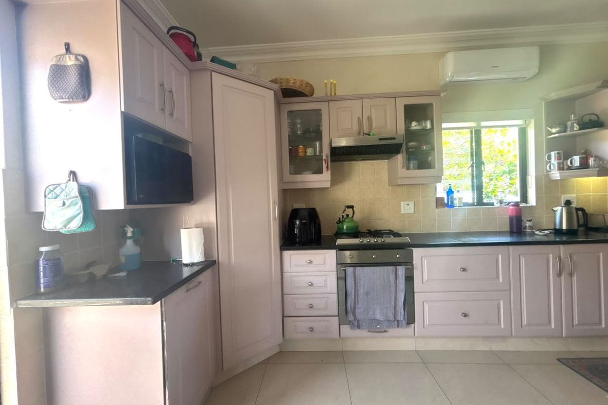 A functional kitchen featuring light-toned cabinetry, a gas hob with extractor fan, built-in oven, and tiled flooring with a split-system air conditioner.