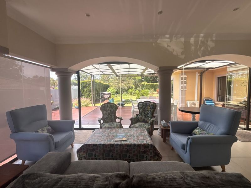 A spacious covered patio featuring structural columns, tiled flooring, and glass sliding doors that open onto a garden area, providing a seamless indoor-outdoor flow.