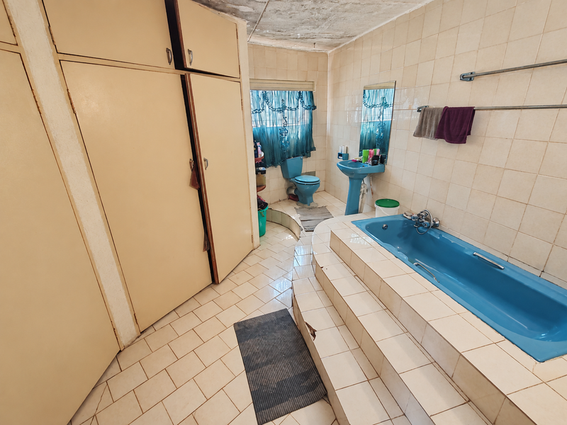 A dated bathroom featuring a sunken blue bathtub, pedestal basin, and built-in storage cupboards, requiring renovation to update the finishes and address tile damage.