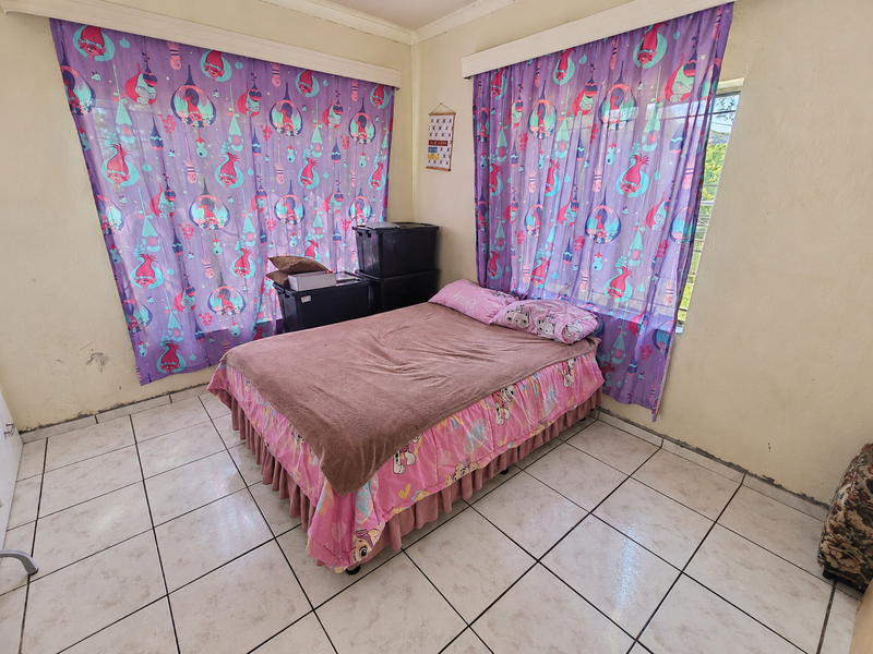 A bedroom featuring tiled flooring and large windows, currently requiring cosmetic updates to the wall finishes to improve the overall aesthetic.